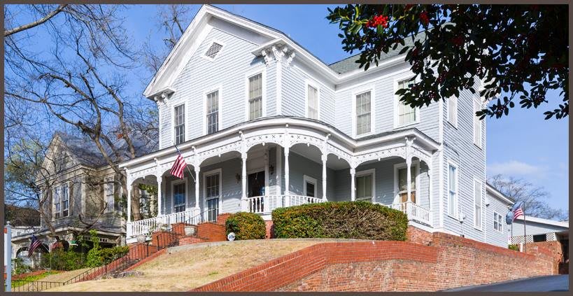 A historic Victorian-style house with a charming porch and an American flag flying out front.