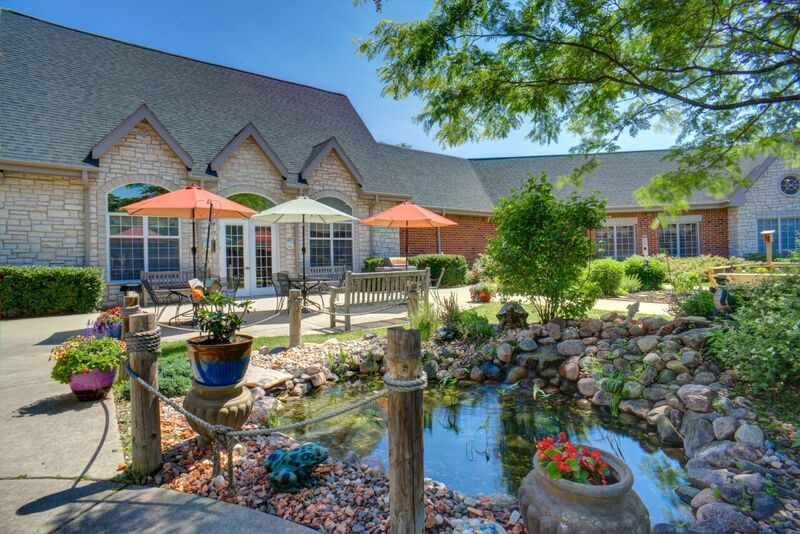 A tranquil garden with a pond, surrounded by patio seating and colorful umbrellas.
