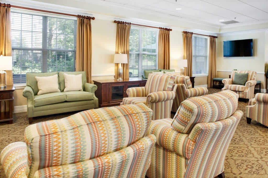 A cozy living room with striped armchairs and a green sofa, accented by warm lighting and large windows.