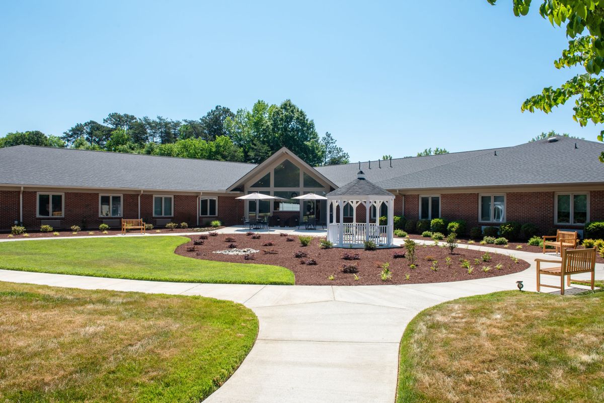 A residential building with a landscaped garden and a central gazebo, surrounded by a pathway on a clear day.