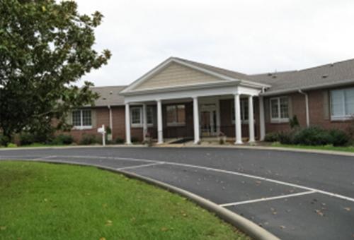 A view of the entrance to a well-maintained building with a landscaped parking area.