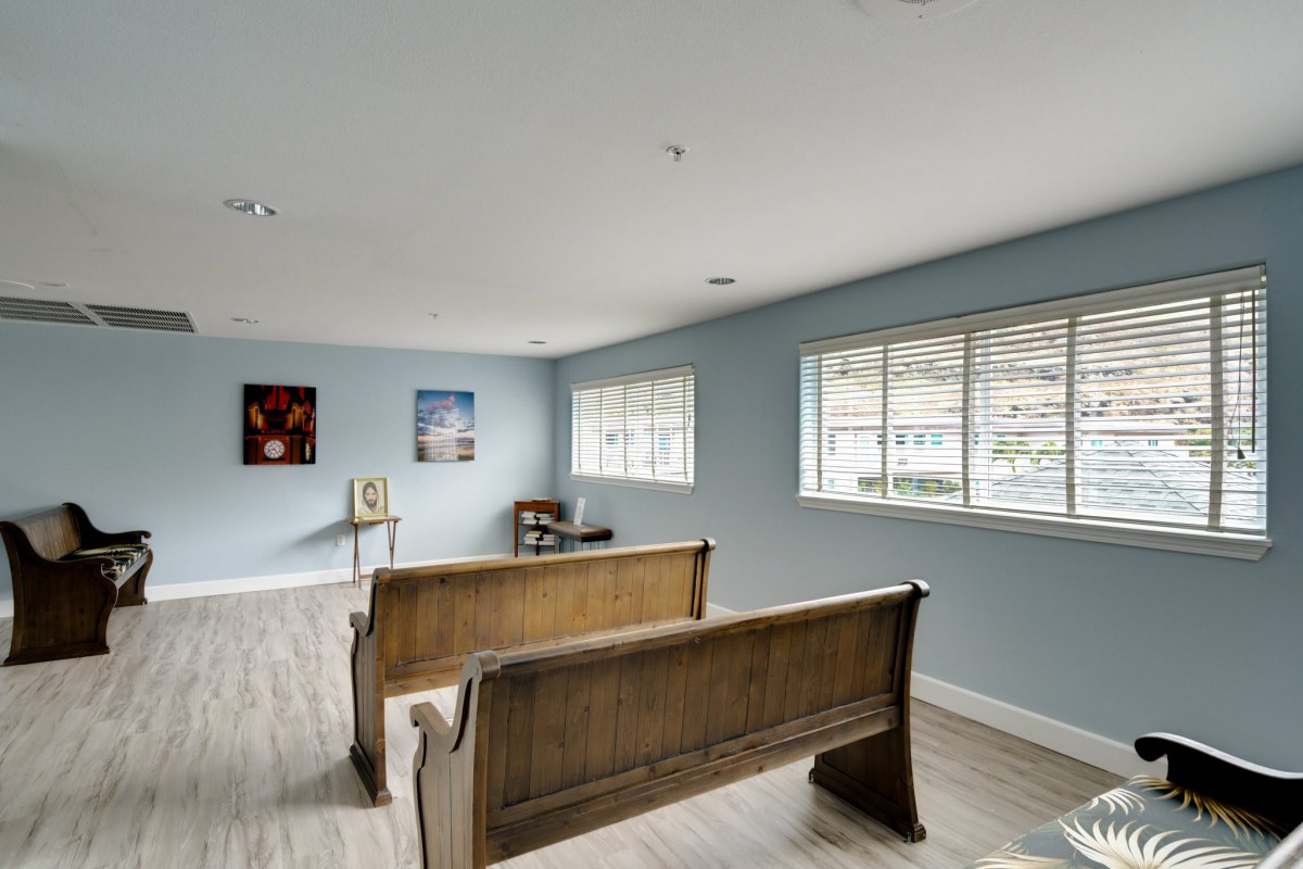A spacious room with wooden benches, light blue walls, and large windows allowing natural light.