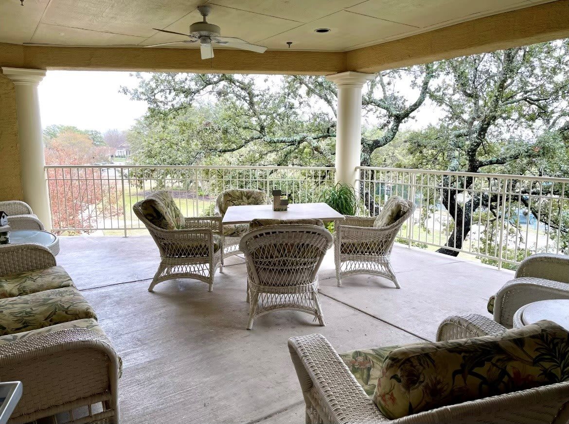 A cozy outdoor patio featuring wicker furniture and a dining table, surrounded by trees.