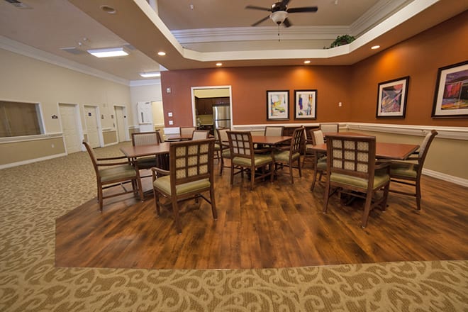 A cozy dining area with wooden flooring, tables and chairs, and warm lighting.