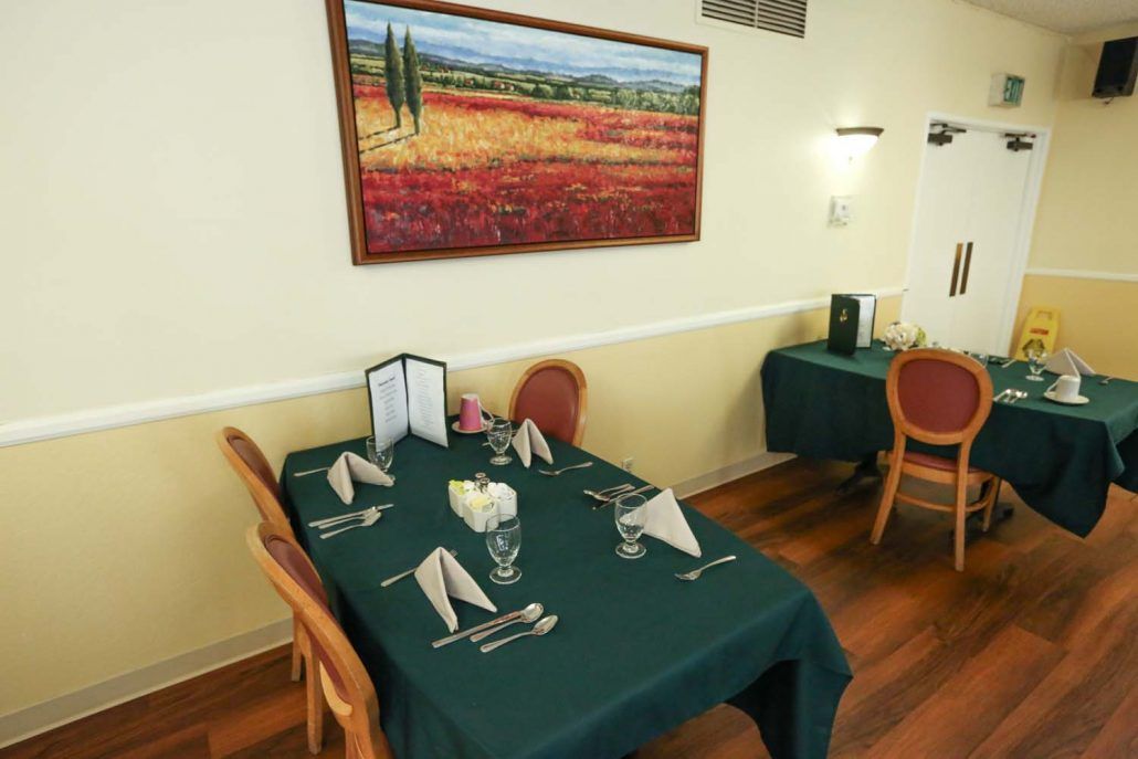 A cozy dining area with neatly set tables and a landscape painting on the wall.