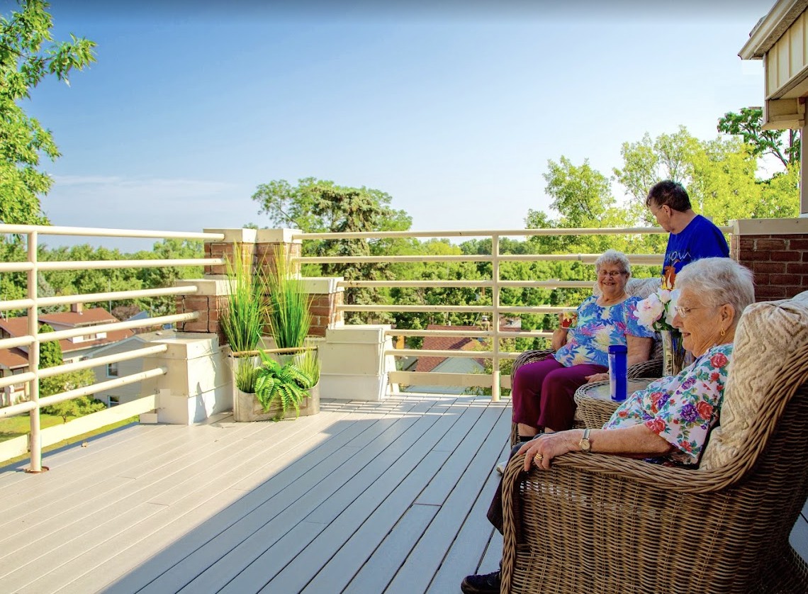 A group of seniors sitting and enjoying the view on a sunny deck surrounded by greenery.
