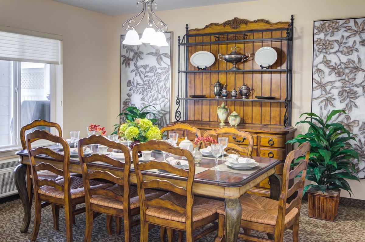 A dining room with a wooden table set for a meal, surrounded by chairs and featuring a decorative cabinet against the wall.