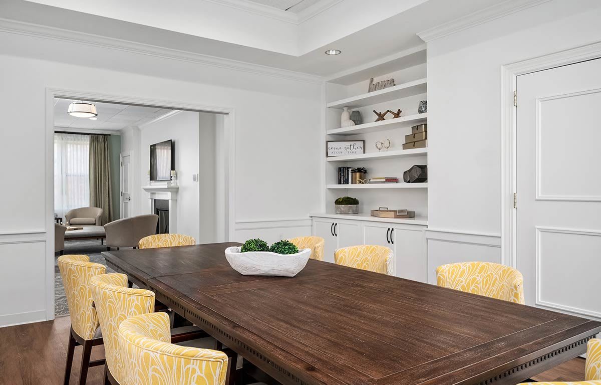 A modern dining room with a wooden table, yellow chairs, and a built-in bookshelf.