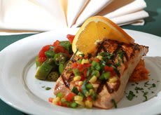 Grilled salmon topped with fresh salsa and served with vegetables, garnished with a slice of citrus.