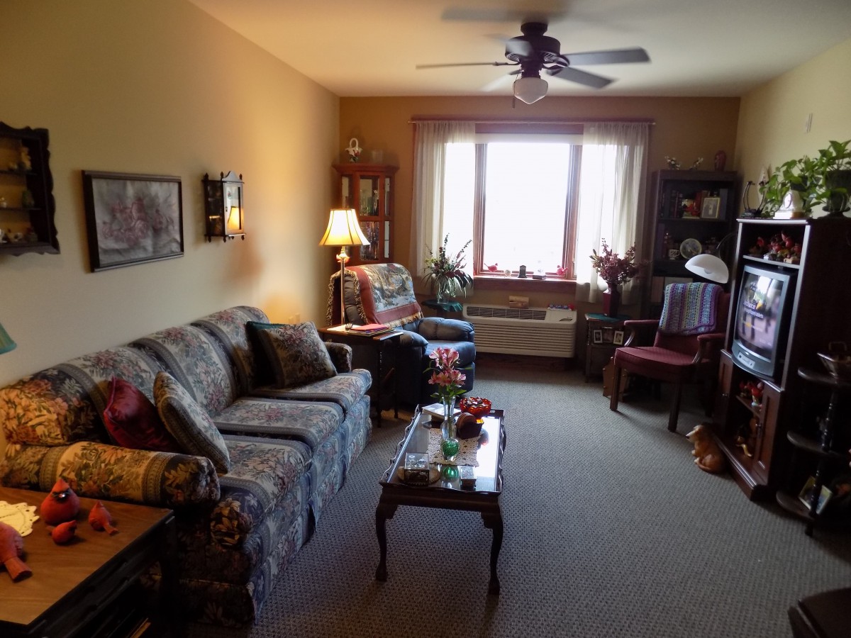 A cozy living room with a sofa, armchair, and coffee table, illuminated by a lamp near the window.