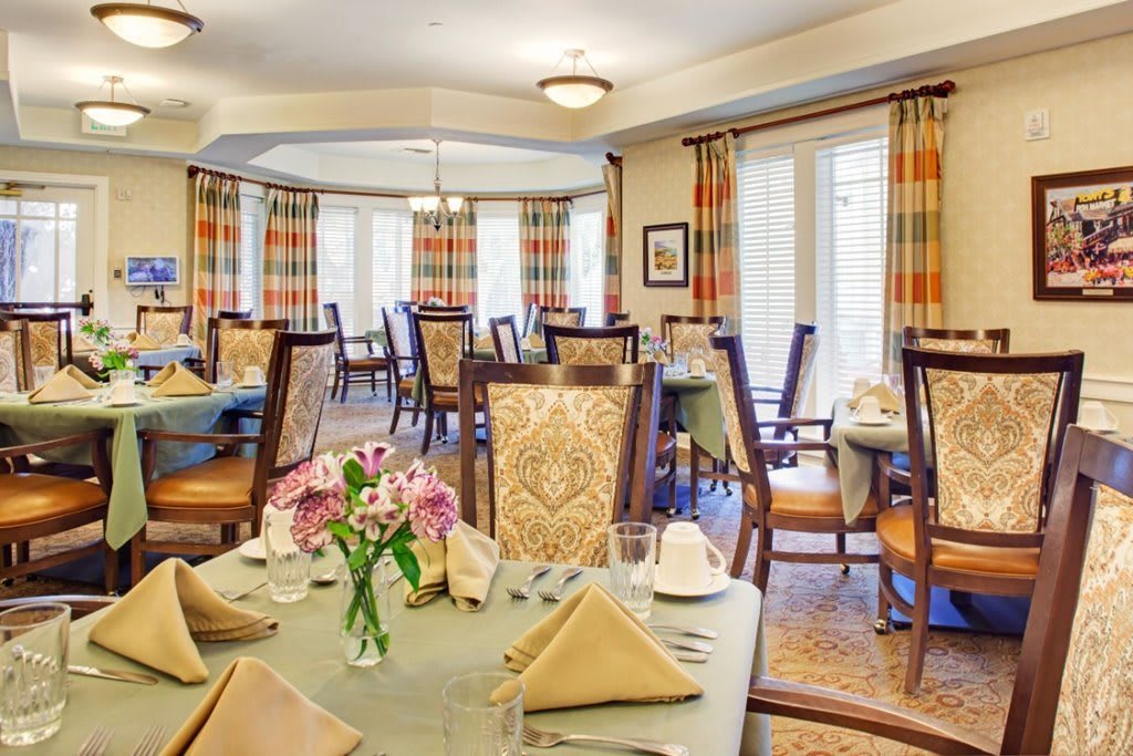 A well-decorated dining room with neatly arranged tables and chairs, featuring elegant decor and fresh flowers.