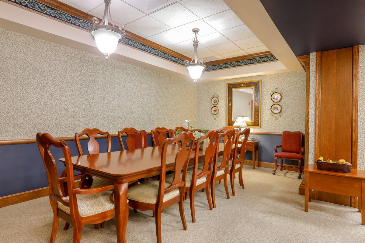 A well-lit dining or conference room with a large wooden table surrounded by chairs and a mirror on the wall.
