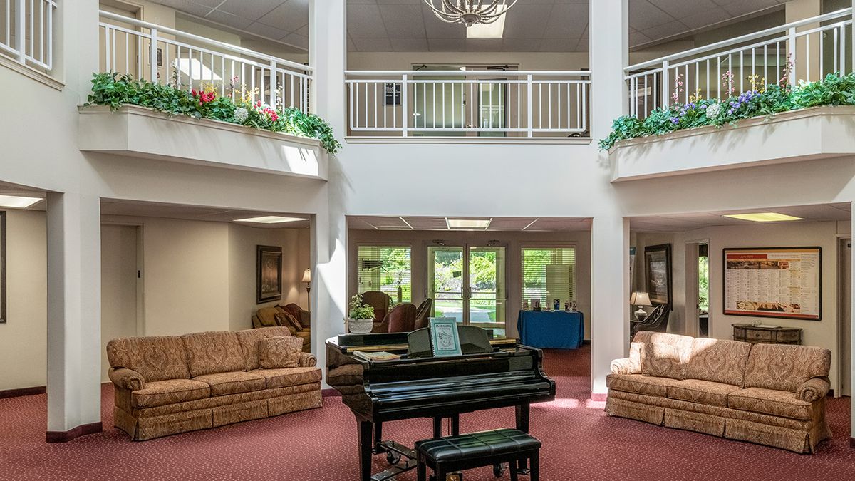 A spacious lobby area featuring a black grand piano, surrounded by comfortable sofas and adorned with indoor plants under a chandelier.