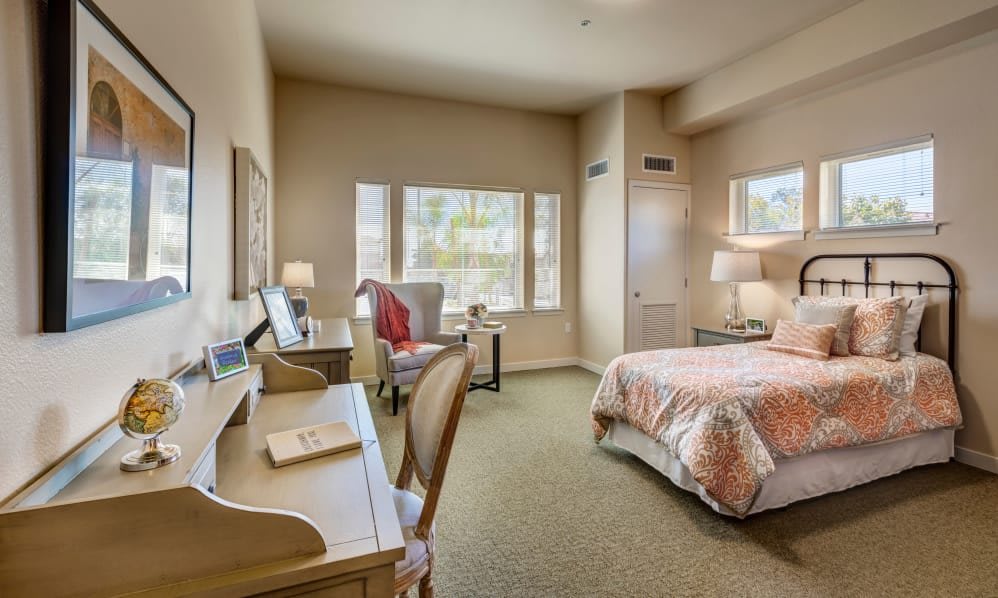 A cozy bedroom with a bed, desk, and large windows letting in natural light.