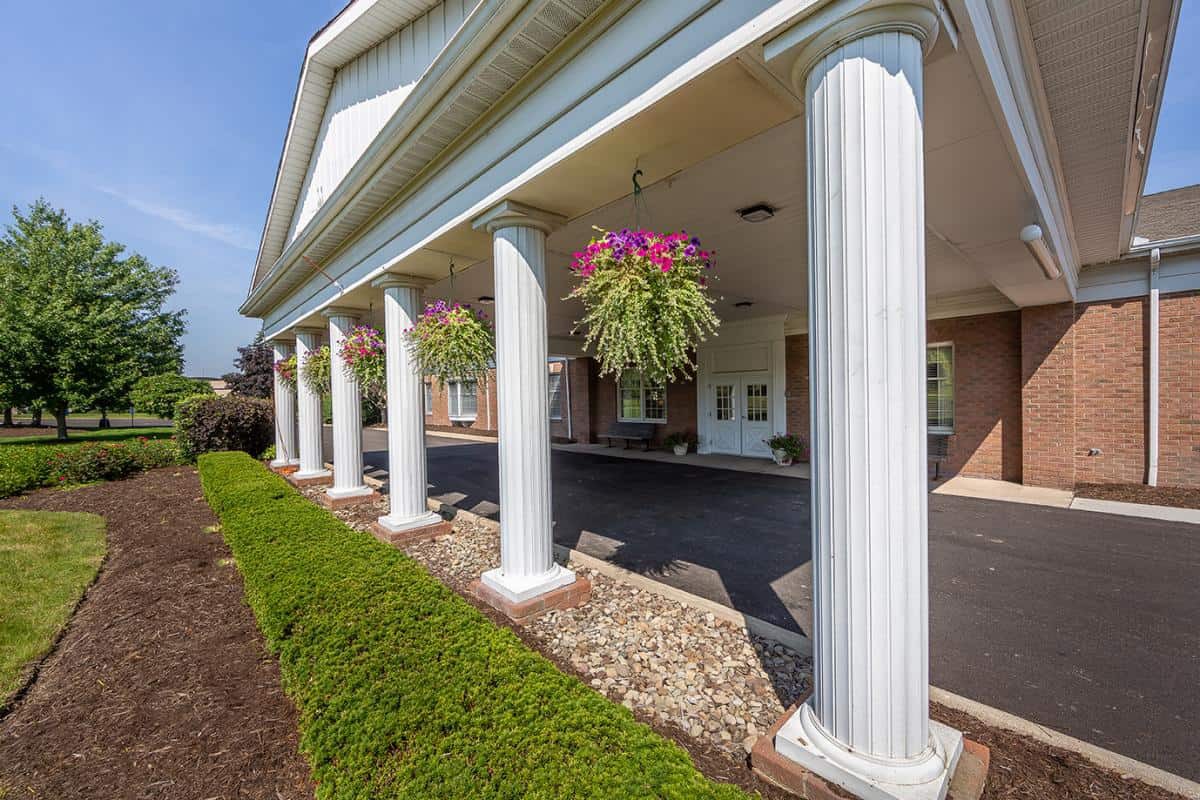 A building with white columns and hanging flower baskets along the entrance walkway.