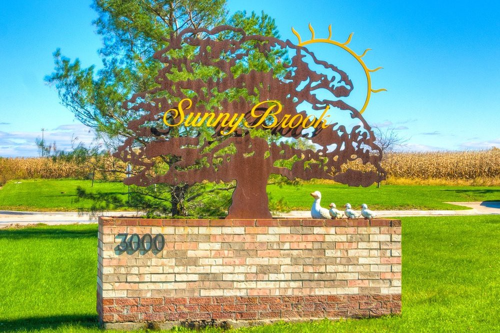 A decorative sign in a park setting, featuring a tree silhouette and the text 'Sunny Bunn' above a brick wall.