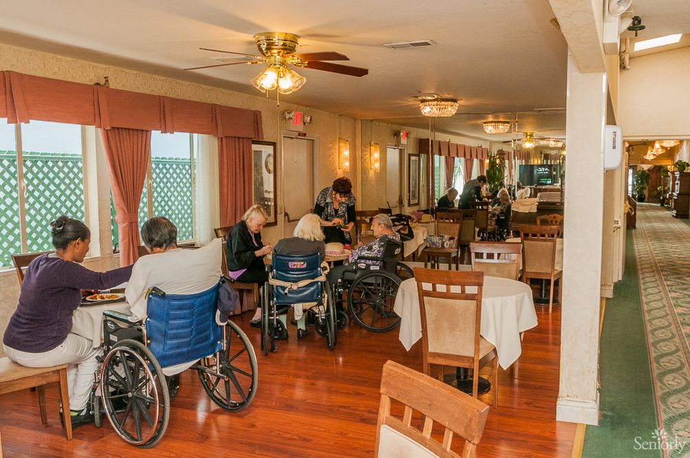 A group of elderly individuals in wheelchairs gathered in a nursing home dining area.