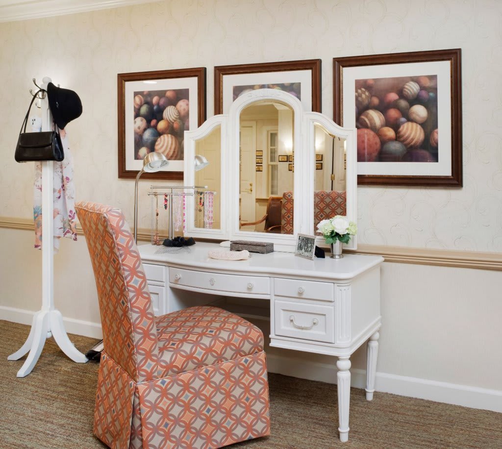 A well-arranged vanity desk with a mirror, stylish chair, and decorative artwork on the wall.