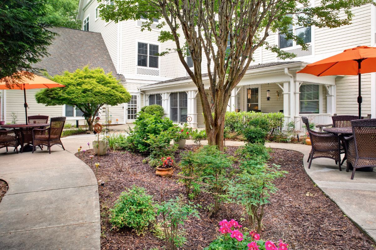 A beautifully landscaped garden with colorful flowers and a tree, surrounded by a pathway in front of a building.