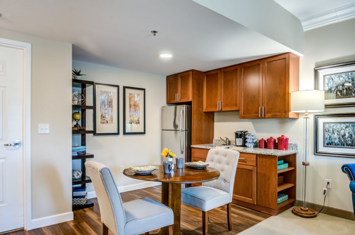 A cozy kitchen and dining area featuring wooden cabinets, modern appliances, and a small round dining table with comfortable chairs.