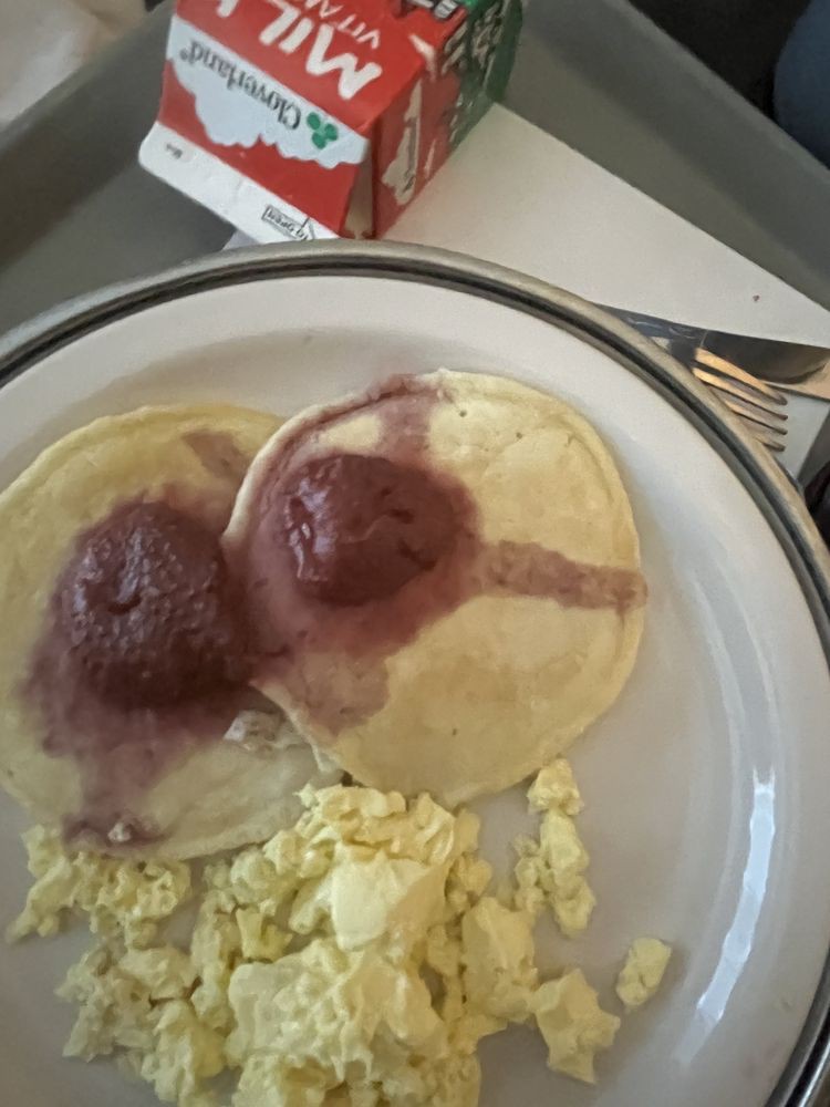 A breakfast plate with pancakes topped with syrup and scrambled eggs.