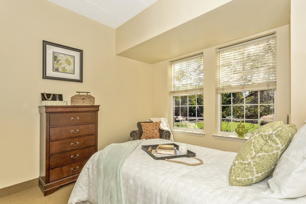 A cozy bedroom with a large window, dresser, and neatly made bed.
