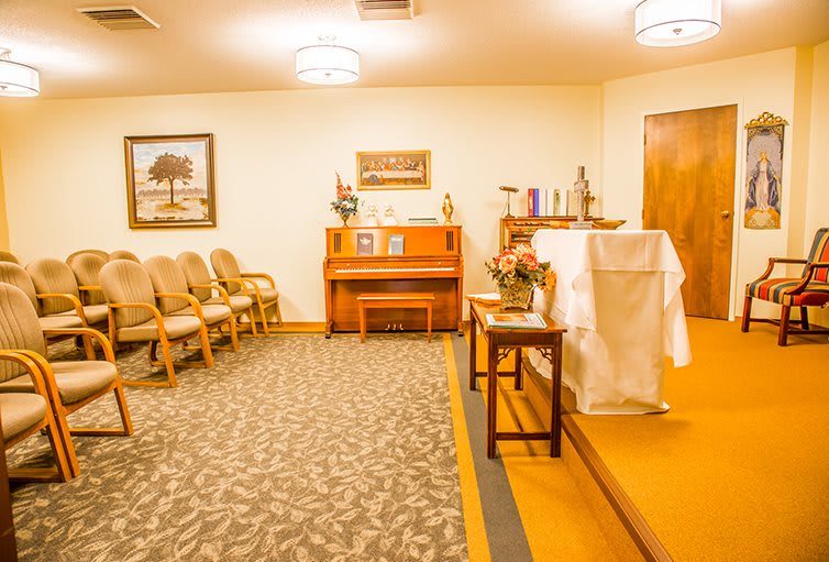 A small chapel interior with a piano, chairs, and a decorated altar.