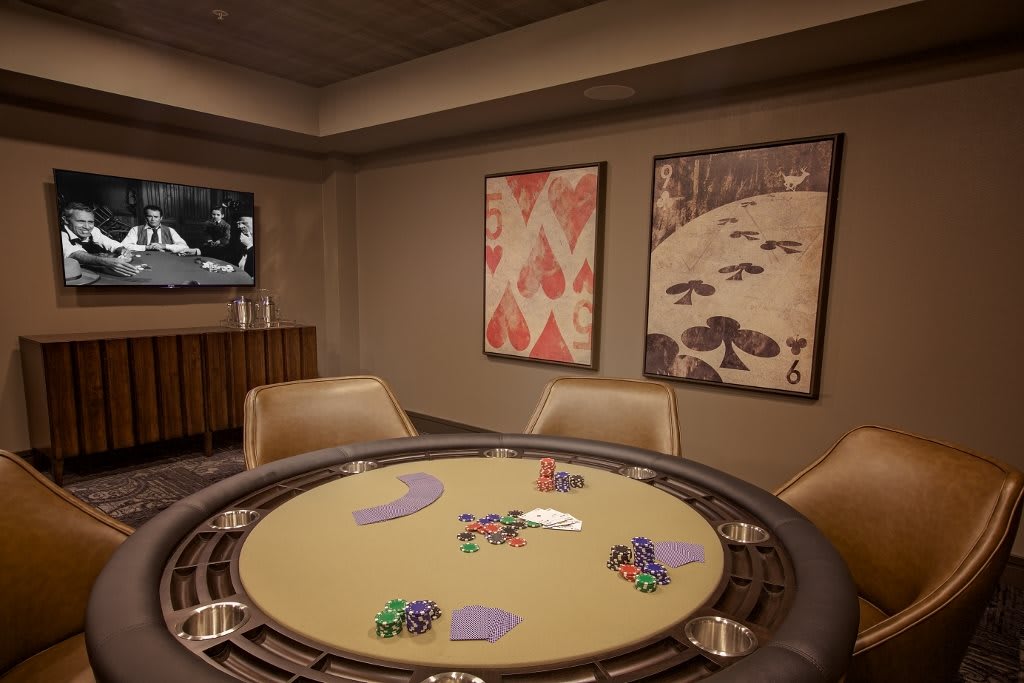 A casino poker room featuring a poker table with chips, surrounded by elegant seating and decorative artwork on the walls.
