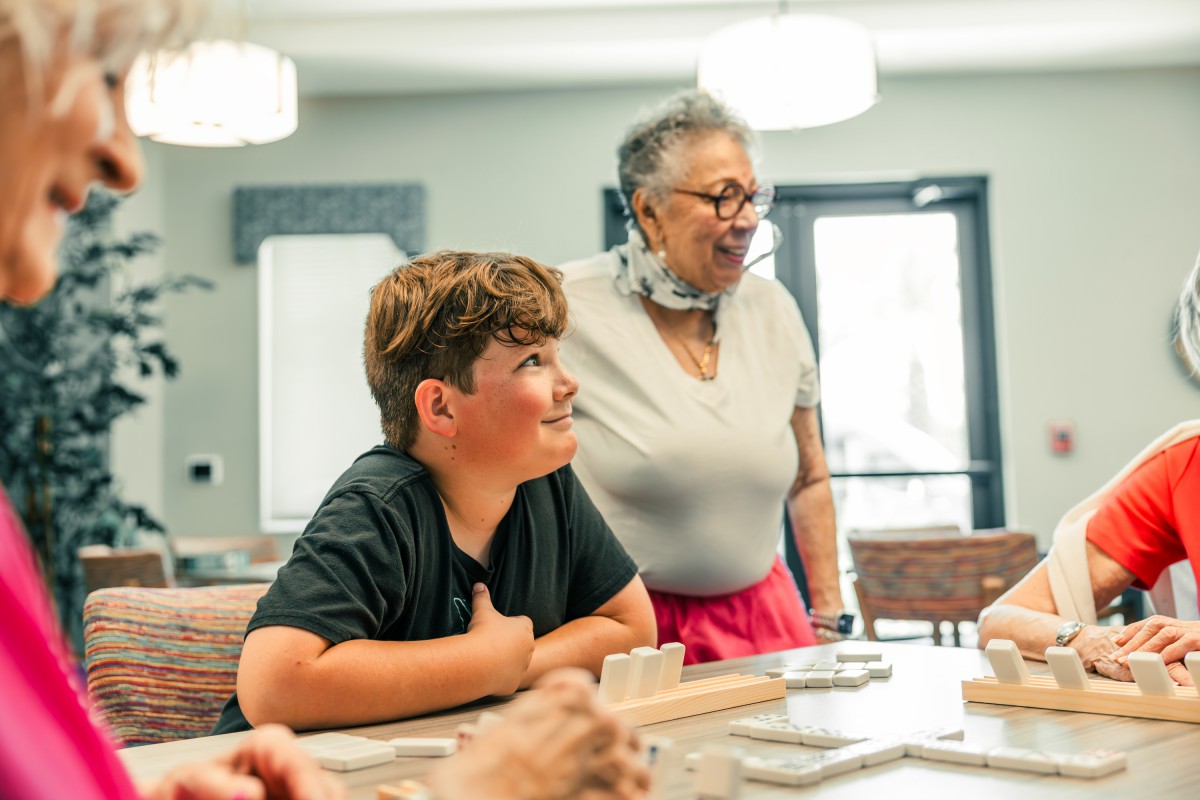A young boy and an older woman enjoy a conversation around a table indoors.