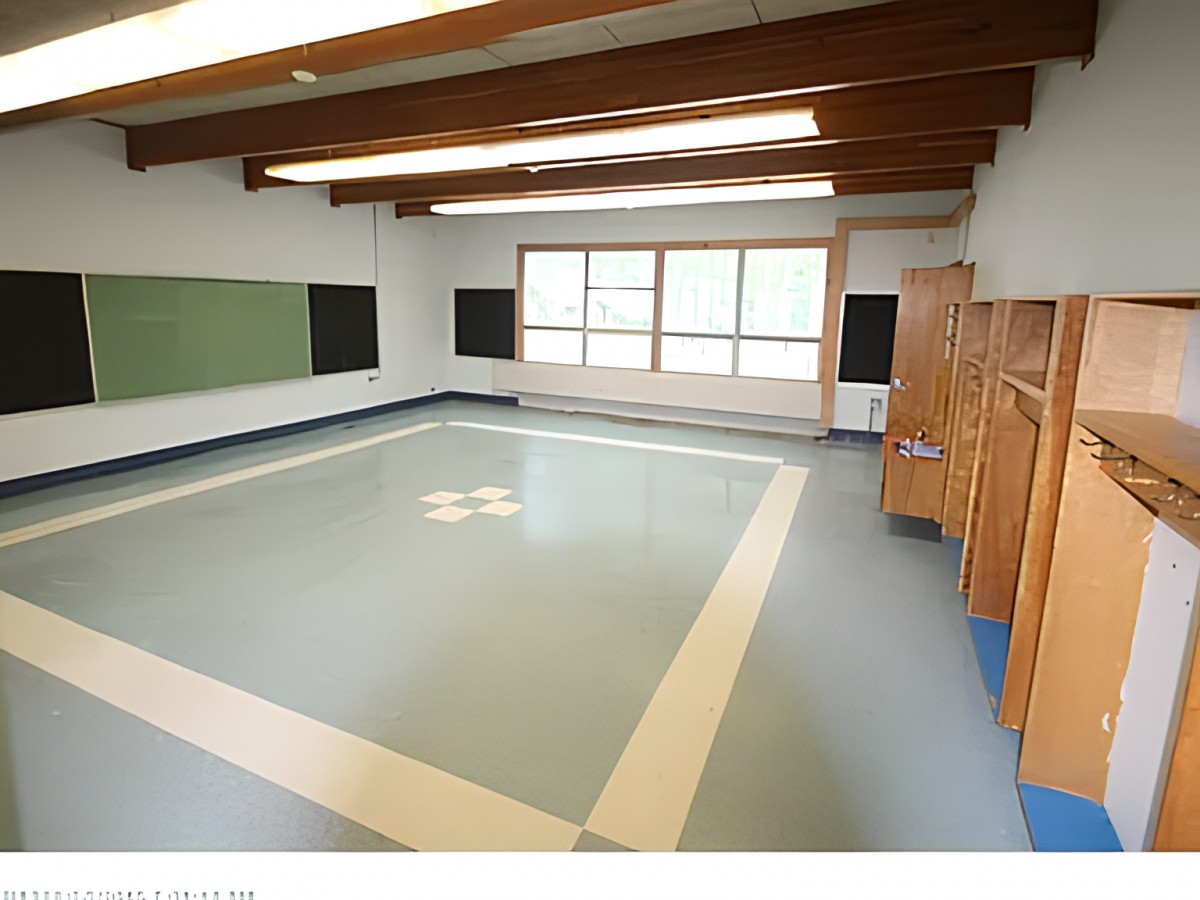 An empty classroom with wooden beams, large windows, and chalkboards.