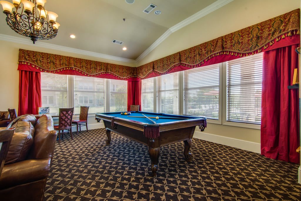 A well-lit game room featuring a pool table with large windows and decorative carpeting.