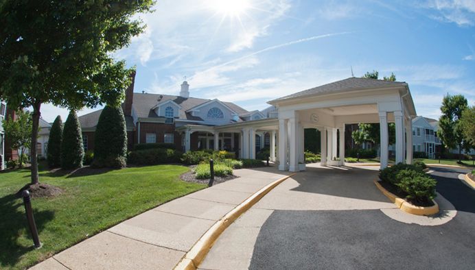 A large residential building with a covered driveway and manicured landscaping under a blue sky.