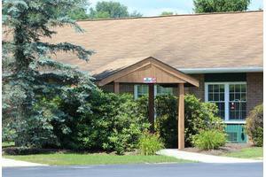 A quaint residential building with a small porch and lush greenery.