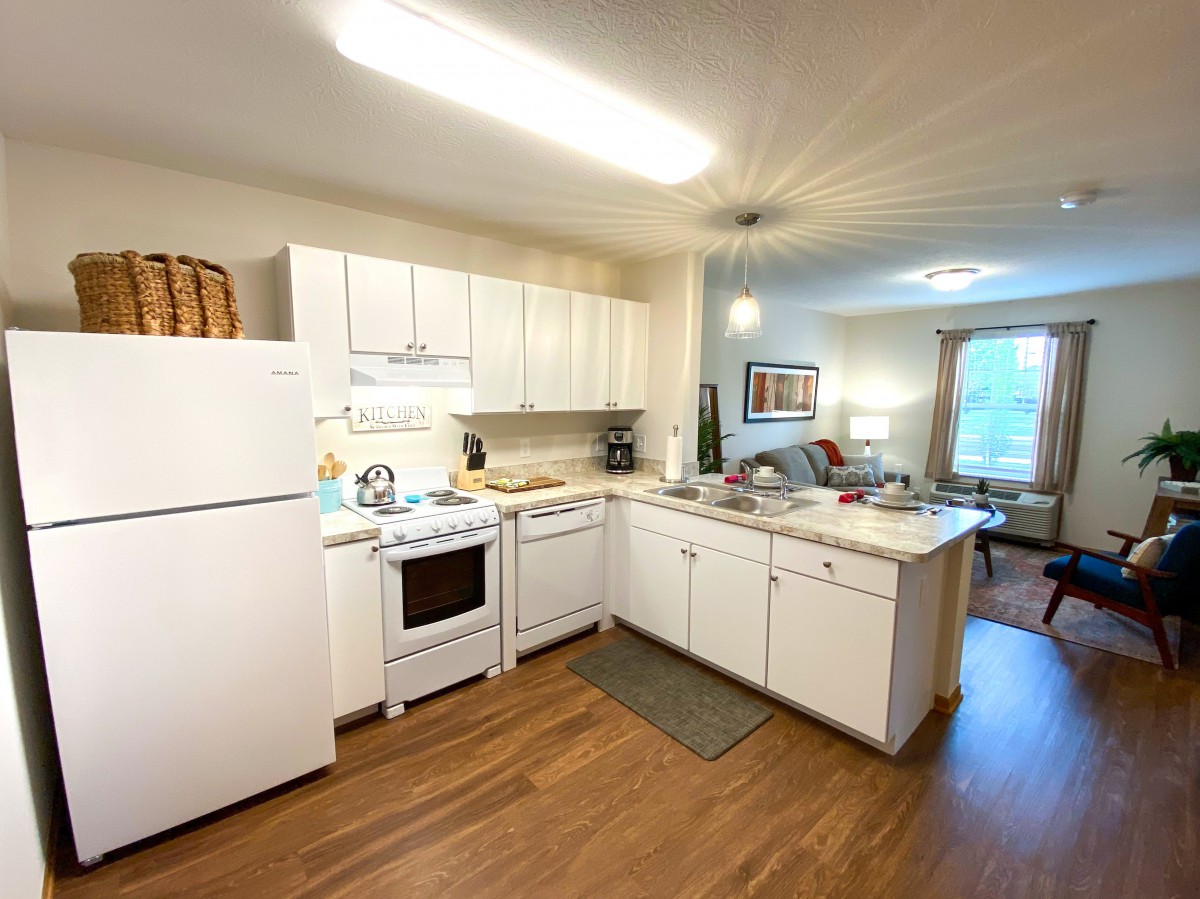 A cozy kitchen with white cabinetry, a refrigerator, and a stove in an apartment setting.