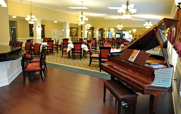 An elegant dining area featuring a grand piano and neatly arranged tables with chairs.