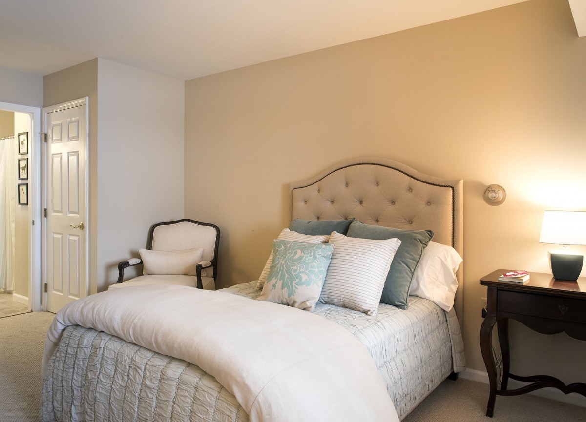 A cozy and elegantly styled bedroom with a bed adorned with multiple pillows, a chair in the corner, and a lamp on a bedside table.