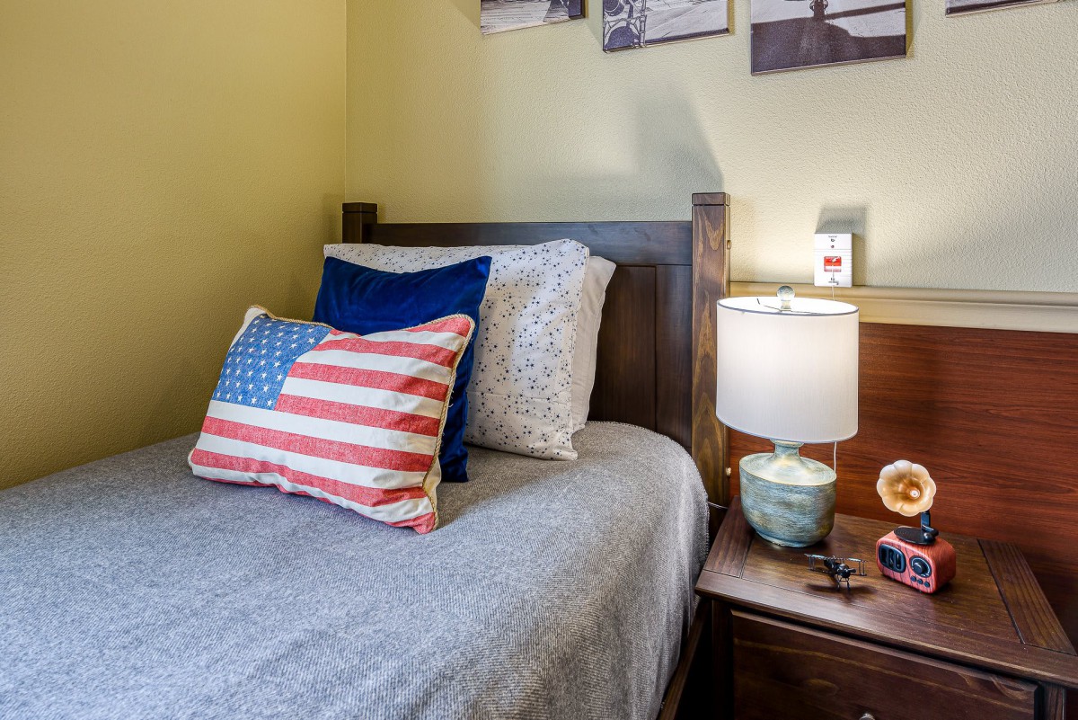 A cozy bedroom setup featuring an American flag pillow, a wooden bed frame, and a lamp on the nightstand.