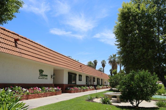 A single-story building surrounded by lush landscaping and palm trees on a sunny day.