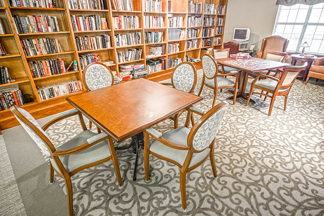A cozy library room featuring wooden tables surrounded by chairs and lined with bookshelves.