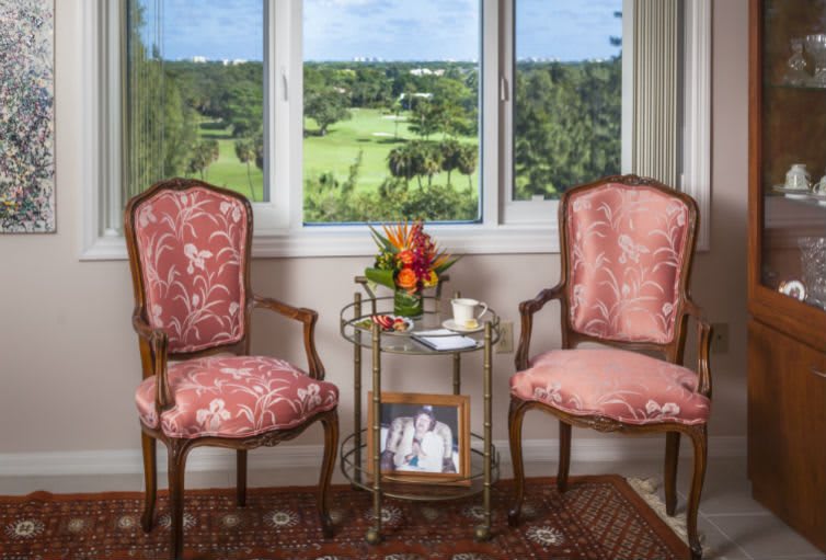 A cozy seating area with two upholstered chairs, a small table holding flowers and a cup, positioned by a window with a scenic view.