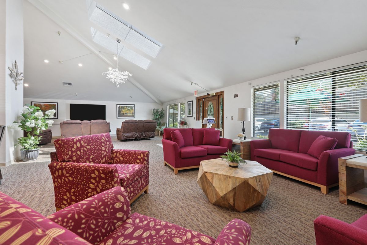A spacious living room featuring red sofas, a geometric coffee table, and a chandelier under a skylight.