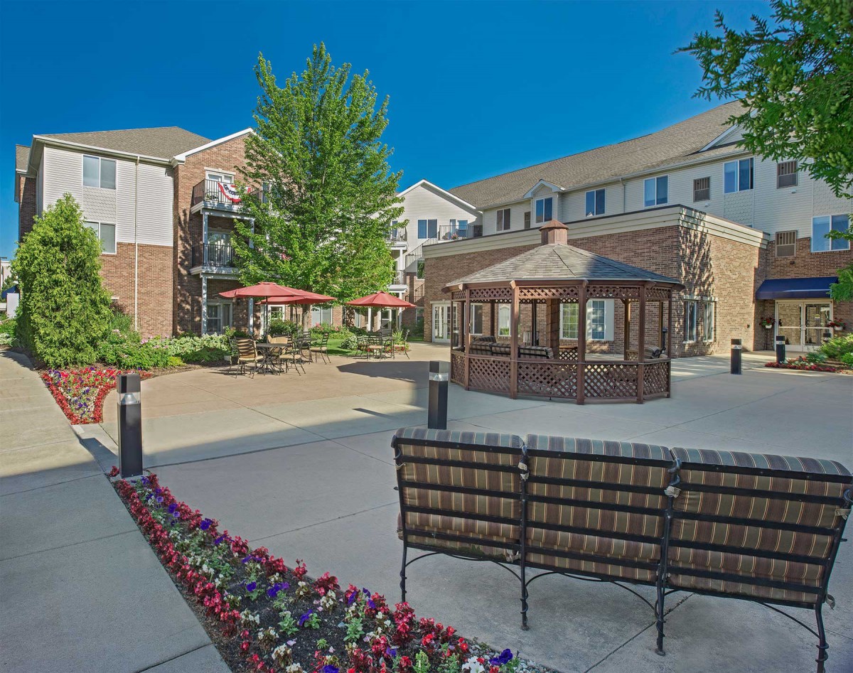 A serene residential courtyard featuring benches, a gazebo, and colorful flower beds.