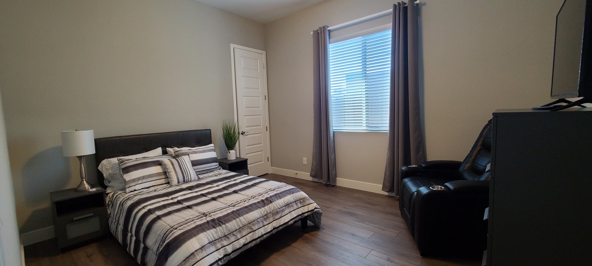 A modern, minimalist bedroom featuring striped bedding and a large window with curtains.