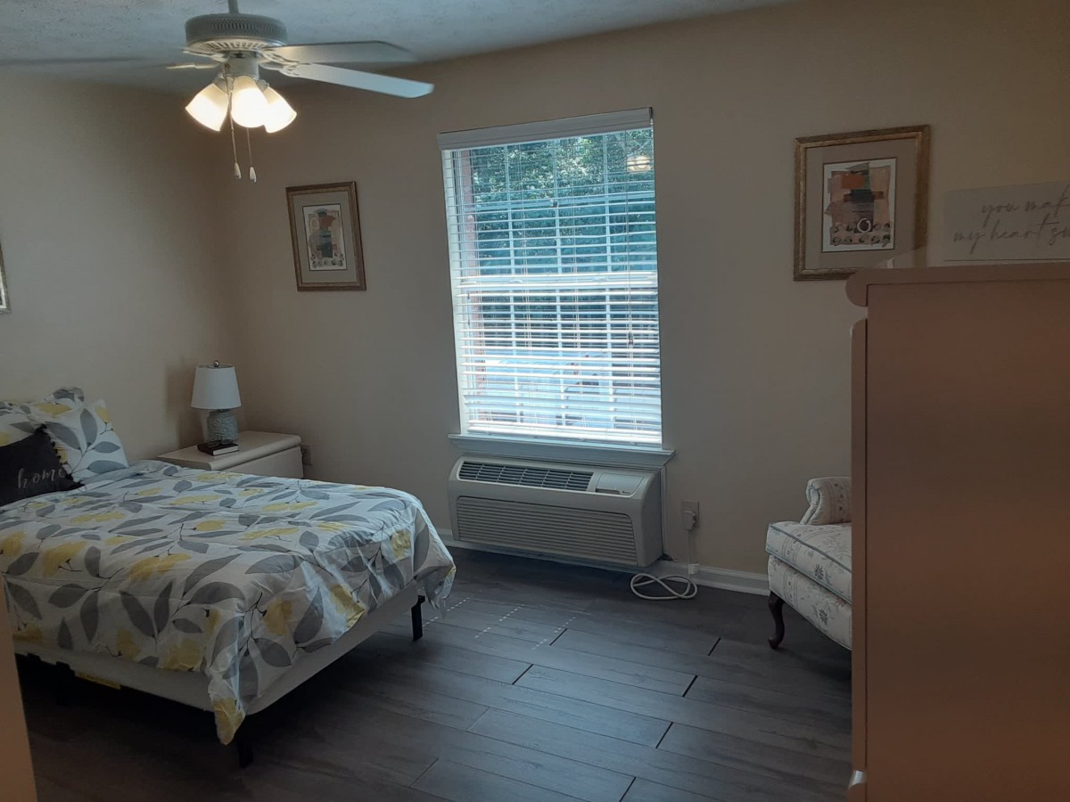 A cozy bedroom with a bed, dresser, and a chair near a window with blinds.