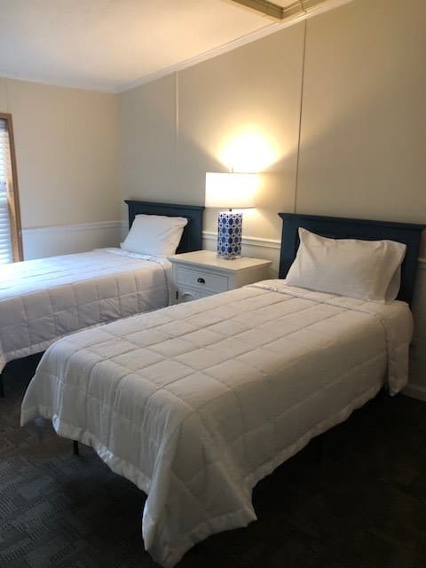 A minimalist bedroom with twin beds and a central nightstand with a lamp.