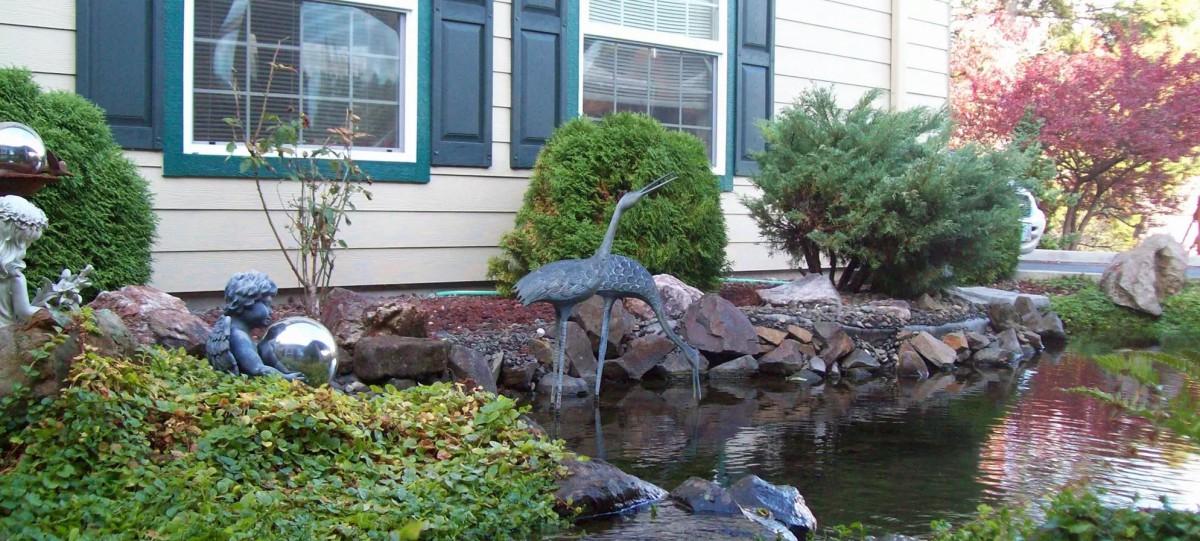 A garden with a pond and a metal bird sculpture in front of a house.
