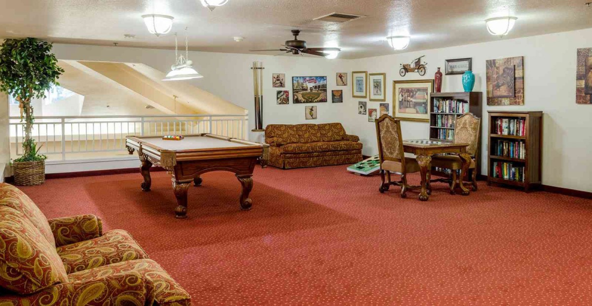 A spacious game room with a billiard table, surrounded by sofas and a small dining setup.
