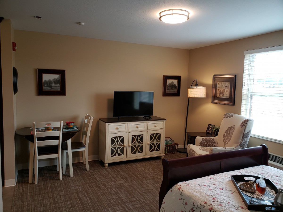 A cozy living room with a TV, table, chair, and lamp.