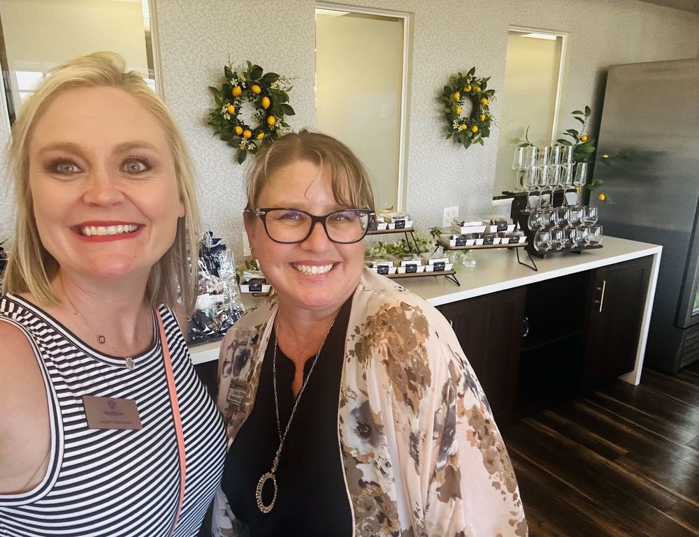 Two women smiling at an indoor event with decorations in the background.