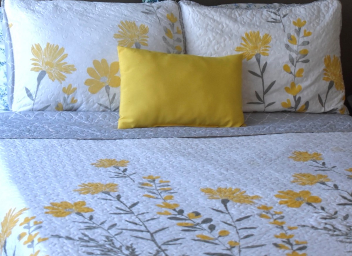 A neatly made bed with yellow floral patterned bedding and a matching decorative pillow.